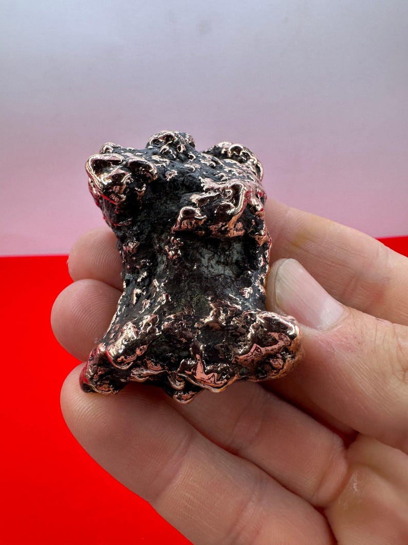 May include: A small, irregularly shaped, copper-colored metal sculpture with a rough, textured surface.