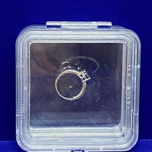 May include: A clear plastic ring box containing a silver ring with a single clear stone.