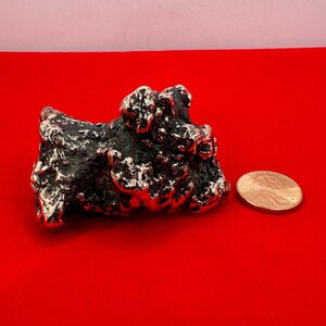 May include: A small, silver, abstract sculpture of a rock formation. The sculpture is about the size of a US penny.
