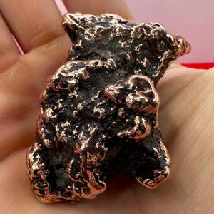 May include: A rough, irregular, copper-colored rock with a textured surface. The rock has a dark brown color with hints of copper.