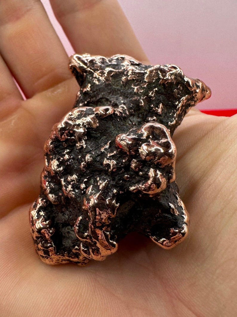 May include: A rough, irregular, copper-colored rock with a textured surface. The rock has a dark brown color with hints of copper.