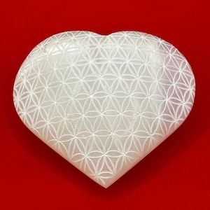 May include: White heart-shaped stone with a carved flower of life pattern.