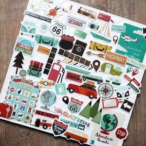 May include: A selection of travel-themed stickers on a white surface. The stickers feature designs such as a Route 66 sign, a vintage camper, a compass, and the words "Road Trip". The color scheme includes teal, red, and gold accents.