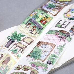 Op de afbeelding: Decoratieve washi tape met aquarel illustraties van interieurscènes met meubels, planten en architecturale details. De tape bevat afbeeldingen van kamers met tafels, stoelen en decoratieve elementen. De tape staat op een witte achtergrond.