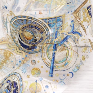 May include: A roll of decorative washi tape featuring a celestial design. The tape showcases intricate illustrations of clocks, planets, and constellations in shades of blue, gold, and white. The tape is ideal for scrapbooking and crafting projects.