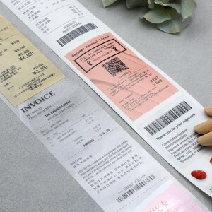 May include: A close-up of a receipt with the text "INVOICE" and "THE CHURCH COFFEE" printed on it. The receipt is on a gray surface. There is a pink baggage removal ticket with a QR code and the text "Baggage Removal Ticket" printed on it. The ticket is on top of the receipt. There is a wooden hand holding the ticket.