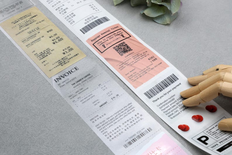 May include: A close-up of a receipt with the text "INVOICE" and "THE CHURCH COFFEE" printed on it. The receipt is on a gray surface. There is a pink baggage removal ticket with a QR code and the text "Baggage Removal Ticket" printed on it. The ticket is on top of the receipt. There is a wooden hand holding the ticket.