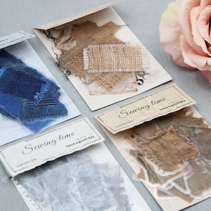 May include: Close-up of four packages of fabric scraps for sewing. The scraps are in shades of blue, brown, and beige. Each package has a label that reads "Sewing time" and "have a good day". A pink rose is in the background.