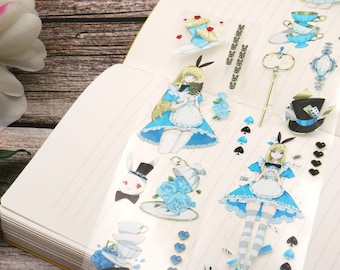 May include: Decorative clear tape featuring illustrations of Alice in Wonderland characters and elements. The tape includes images of Alice, a white rabbit, teacups, playing cards, and other themed graphics in blue, white, and gold.
