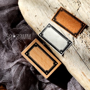 May include: Three wooden stamps with black frames and decorative corners. The stamps are rectangular and measure 50 x 30 mm. The stamps are on a wooden surface.