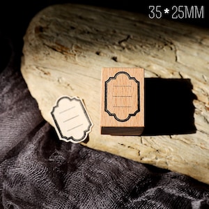 May include: A wooden stamp with a black frame and three lines inside. The stamp is 35 mm by 25 mm and is on a wooden surface. The text "35 * 25MM" is visible in the image.