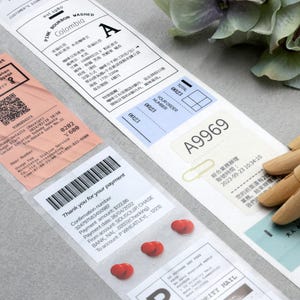 May include: A close-up of various labels and stickers, including a pink baggage removal ticket with a QR code, a white label with the text "PINE BOURBON WASHED Colombia A", a blue label with the text "A9969", and a white label with a barcode and the text "Thank you for your payment".