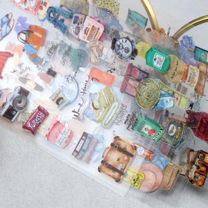 May include: A sheet of colorful stickers featuring travel-themed illustrations. The stickers include a camera, luggage, handbags, a watch, and food items. The stickers are on a clear background with handwritten text.