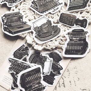 May include: A collection of vintage typewriter stickers in black and white. The stickers are printed on white paper and have a distressed look. The stickers feature different types of typewriters, including a manual typewriter, an electric typewriter, and a portable typewriter.