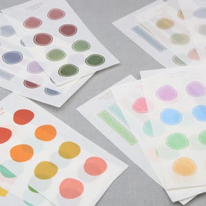May include: Sheets of stickers with colorful, abstract shapes. Each sheet features a different color palette, including red, orange, yellow, green, blue, and purple. The text "COLOR FOR" is visible on some sheets.
