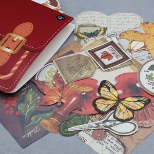 May include: A collection of vintage-style paper ephemera, including a red paper purse, butterfly and leaf cutouts, and botanical illustrations. The items are in shades of red, brown, and yellow, with a touch of gold.