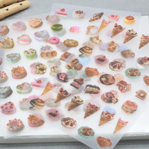 May include: Sheets of stickers featuring various miniature desserts, including cakes, ice cream cones, and pastries. The stickers showcase a variety of colors and designs, perfect for crafting or decorating. The stickers are on a clear backing.