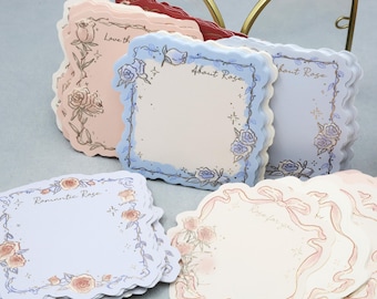 May include: A collection of decorative paper notes with scalloped edges. The notes feature floral illustrations of roses and text such as "About Rose" and "Romantic Rose". The color palette includes soft pinks, blues, and cream.