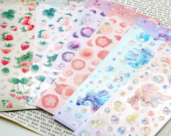 May include: A set of six sheets of colorful, iridescent stickers featuring various designs. The stickers include strawberries, flowers, and fish in a bubble design. The stickers are perfect for adding a touch of whimsy to journals, planners, and other craft projects.
