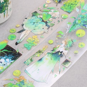 May include: Decorative washi tape featuring illustrations of figures in flowing gowns, flowers, and foliage in shades of green, blue, and yellow. The tape has a transparent background and is partially rolled.