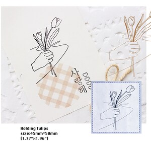 Peut inclure: Dessin au trait minimaliste d'une main tenant des tulipes. L'image comprend le texte "Holding Tulips" et les dimensions : 4,5 cm x 5 cm. Un autocollant en forme de cœur avec du texte coréen et un motif à carreaux est également présent.