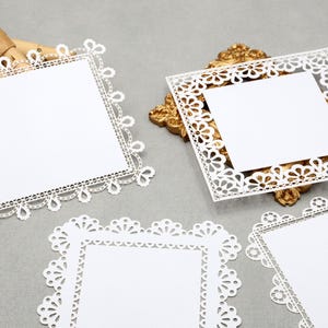 May include: White, square paper doilies with intricate lace-like edges. Some are placed on a gold-colored decorative frame. The doilies are blank in the center, ready for customization. The overall theme is crafting and DIY projects.