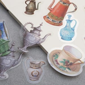 May include: A set of vintage-style teacups, teapots, and other tableware stickers. The stickers feature intricate designs and patterns in shades of blue, green, pink, and gold.