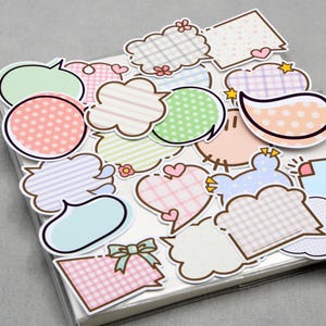 May include: A collection of colorful speech bubble stickers in various shapes and patterns, including polka dots, stripes, and plaid. The stickers are in pastel colors like pink, green, and blue, with black outlines. They are arranged on a white surface.