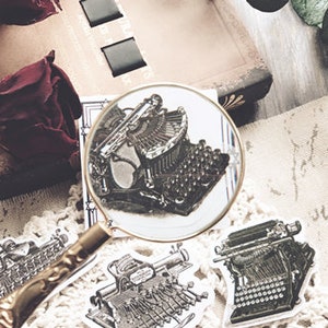 May include: A close-up of a vintage typewriter sticker with a magnifying glass over it. The sticker is on a white background with other vintage typewriter stickers.