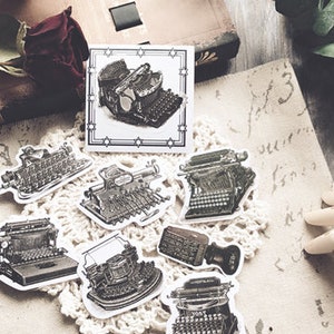May include: A set of vintage typewriter stickers in black and white. The stickers are on a white background with a lace doily underneath. The stickers are perfect for adding a vintage touch to your journals, planners, or scrapbooks.