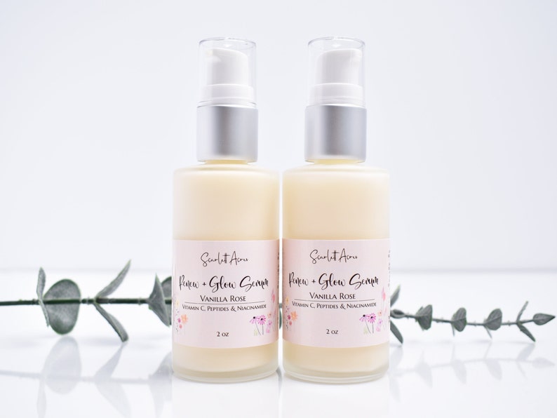 May include: Two 2-ounce bottles of serum labeled "Renew + Glow Serum" in a white and pink font. The bottles are clear and contain a white liquid. The label also says "Vanilla Rose" and lists ingredients including Vitamin C, Peptides, and Niacinamide.