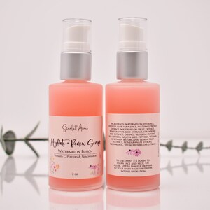 Op de afbeelding: Twee flessen roze serum van 2 ounce met het label "Hydrate + Renew Serum Watermelon Fusion Vitamin C, Peptides & Niacinamide".