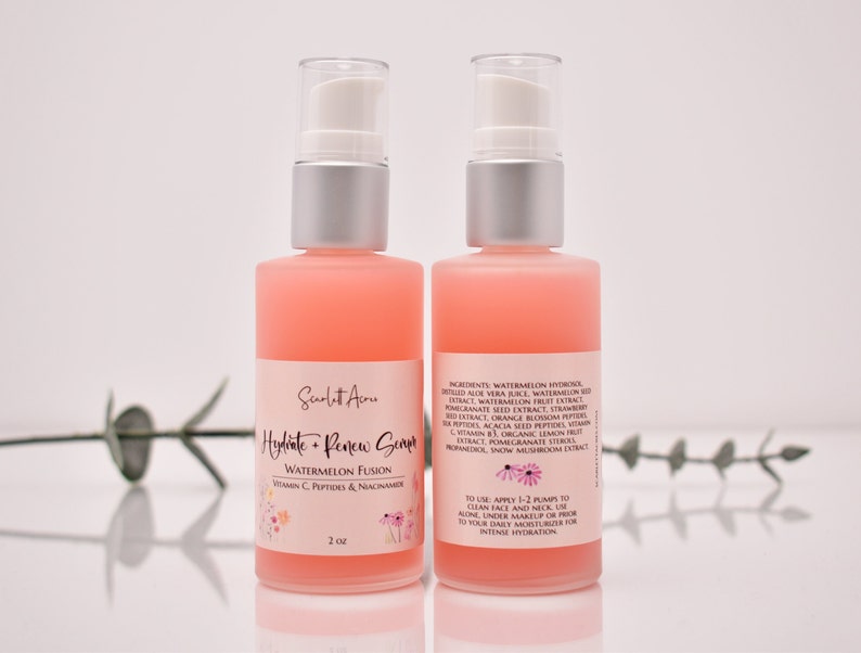 Op de afbeelding: Twee flessen roze serum van 2 ounce met het label "Hydrate + Renew Serum Watermelon Fusion Vitamin C, Peptides & Niacinamide".