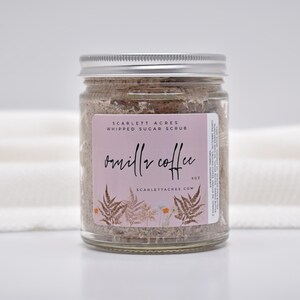 May include: A clear glass jar filled with brown whipped sugar scrub, topped with a silver metal lid. The label features a light pink background, the text Scarlett Acres Whipped Sugar Scrub, Vanilla Coffee, 9oz, and botanical fern illustrations.
