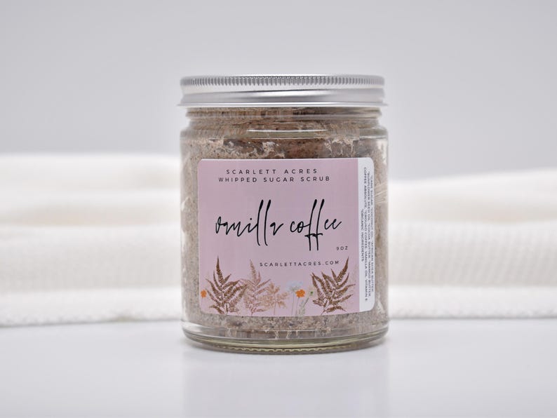 May include: A clear glass jar filled with brown whipped sugar scrub, topped with a silver metal lid. The label features a light pink background, the text Scarlett Acres Whipped Sugar Scrub, Vanilla Coffee, 9oz, and botanical fern illustrations.