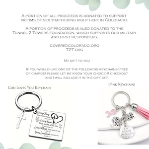 May include: Two metal keychains: one rectangular silver-toned tag with a cross charm and religious text, and one silver-toned ring with a pink tassel, a pink ribbon charm, a tree charm, a heart charm, and a round tag reading She believed she could so she did.