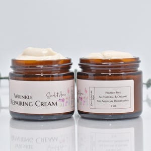May include: Two amber glass jars of wrinkle repairing cream with white labels. The label on the left jar reads "Wrinkle Repairing Cream" and "Scarlet Rose". The label on the right jar reads "Dry/Mature Skin", "Paraben Free", "All Natural & Organic", "No Artificial Preservatives", and "2 oz".