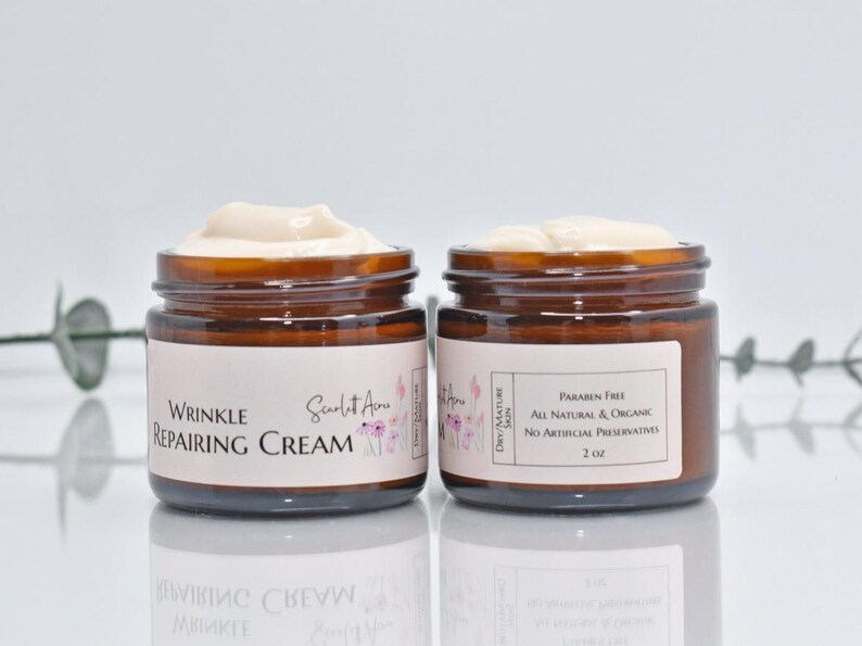 May include: Two amber glass jars of wrinkle repairing cream with white labels. The label on the left jar reads "Wrinkle Repairing Cream" and "Scarlet Rose". The label on the right jar reads "Dry/Mature Skin", "Paraben Free", "All Natural & Organic", "No Artificial Preservatives", and "2 oz".