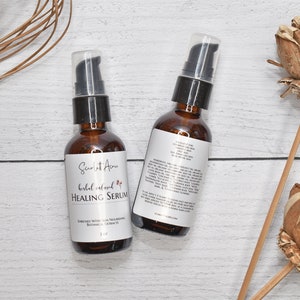 May include: Two amber glass bottles with black pump tops filled with a herbal infused healing serum. The bottles are labeled "Scarlet Acres Herbal Infused Healing Serum" and have a list of ingredients on the back. The bottles are sitting on a white wooden surface.