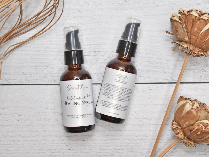May include: Two amber glass bottles with black pump tops filled with a herbal infused healing serum. The bottles are labeled "Scarlet Acres Herbal Infused Healing Serum" and have a list of ingredients on the back. The bottles are sitting on a white wooden surface.