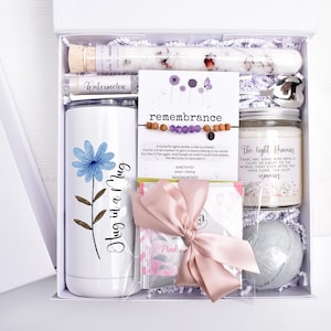 Puede incluir: Una caja de regalo blanca llena de art&iacute;culos de cuidado personal. Incluye un vaso con una flor azul y el texto "Hug in a Mug", una vela, una bomba de ba&ntilde;o, una pulsera, sales de ba&ntilde;o y un b&aacute;lsamo labial.