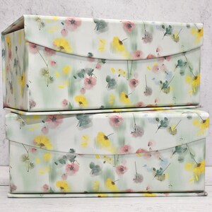 May include: Two stackable storage boxes with a floral pattern. The boxes are white with a green, yellow, and pink floral design.
