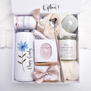 May include: A white gift box labeled Option 1 containing a white tumbler with a blue flower and the text Nurse Emily, a lotion bottle, a heart-shaped spoon, a bath bomb, a candle with text, a lip balm, a jewelry box, and a bar of soap with a ribbon.