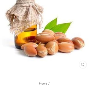 May include: A glass bottle of Moroccan argan oil with a burlap covering and a pile of argan nuts in front of it.