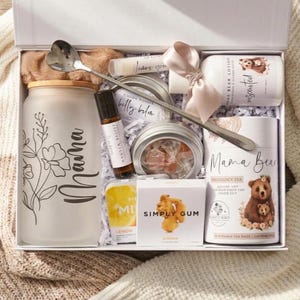 May include: A gift box containing a frosted glass tumbler with a bamboo lid and floral Mama text, a heart-shaped spoon, a roller bottle, belly balm, unscented lotion with a pink ribbon, Simply Gum ginger mints, and a Mama Bear pregnancy tea canister.