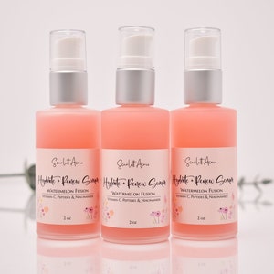 Op de afbeelding: Drie roze glazen flessen met zilveren pompjes en witte etiketten. De etiketten lezen "Hydrate + Renew Serum" met de tekst "Watermelon Fusion" en "Vitamin C, Peptides & Niacinamide" eronder. Elke fles bevat 60 ml serum.