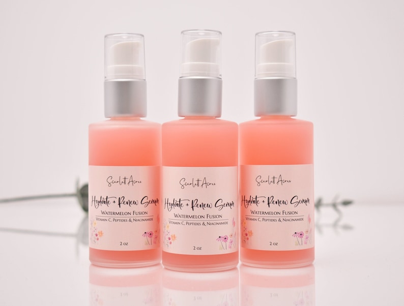 Op de afbeelding: Drie roze glazen flessen met zilveren pompjes en witte etiketten. De etiketten lezen "Hydrate + Renew Serum" met de tekst "Watermelon Fusion" en "Vitamin C, Peptides & Niacinamide" eronder. Elke fles bevat 60 ml serum.