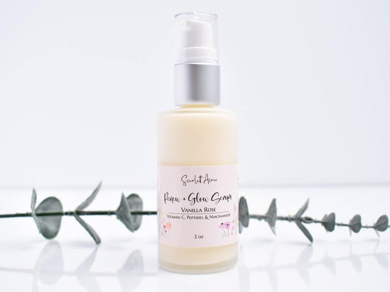 May include: A clear glass bottle with a silver pump top filled with a white lotion. The bottle label is pink and says "Scarlet Acne Renew + Glow Serum Vanilla Rose Vitamin C, Peptides & Niacinamide 2 oz".