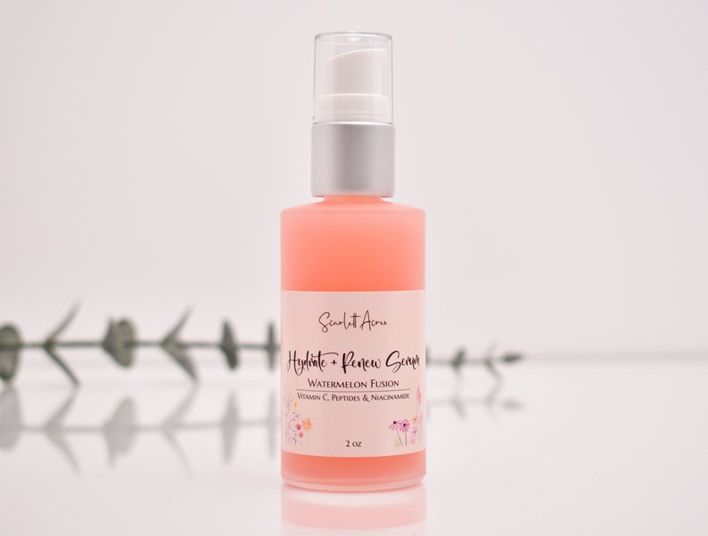 Op de afbeelding: Een roze glazen fles met een witte pomp en een etiket met de tekst "Hydrate + Renew Serum Watermeloen Fusion Vitamine C, Peptiden & Niacinamide 2 oz".