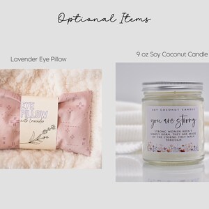 May include: A dusty pink lavender eye pillow with a cream-colored label reading EYE PILLOW with Lavender and a 9 oz soy coconut candle in a glass jar with a label reading you are strong STRONG WOMEN AREN'T SIMPLY BORN. THEY ARE MADE OF THE STORMS THEY WALK THROUGH.